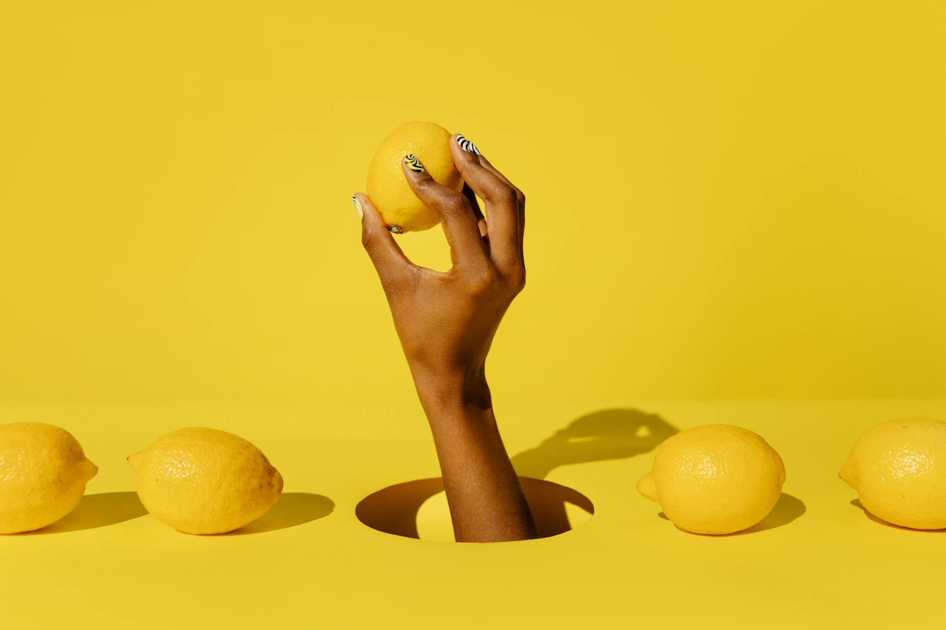 A hand holding a fresh lemon against a vivid yellow background, symbolizing the cyclical nature of sensation and pleasure
