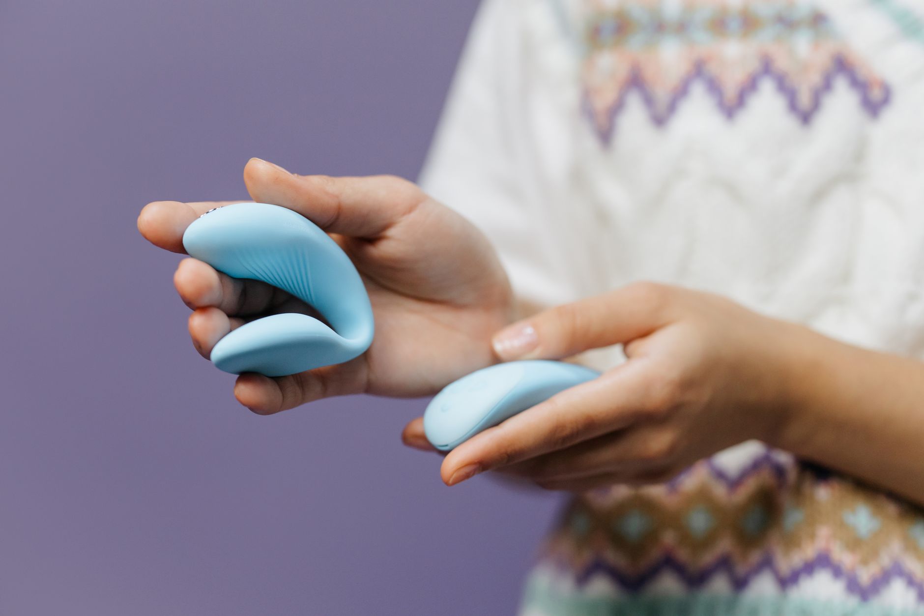 Close-up of hands holding a sleek clitoral vibrator against a purple background, symbolizing intimate pleasure and self-care in long-term relationships.