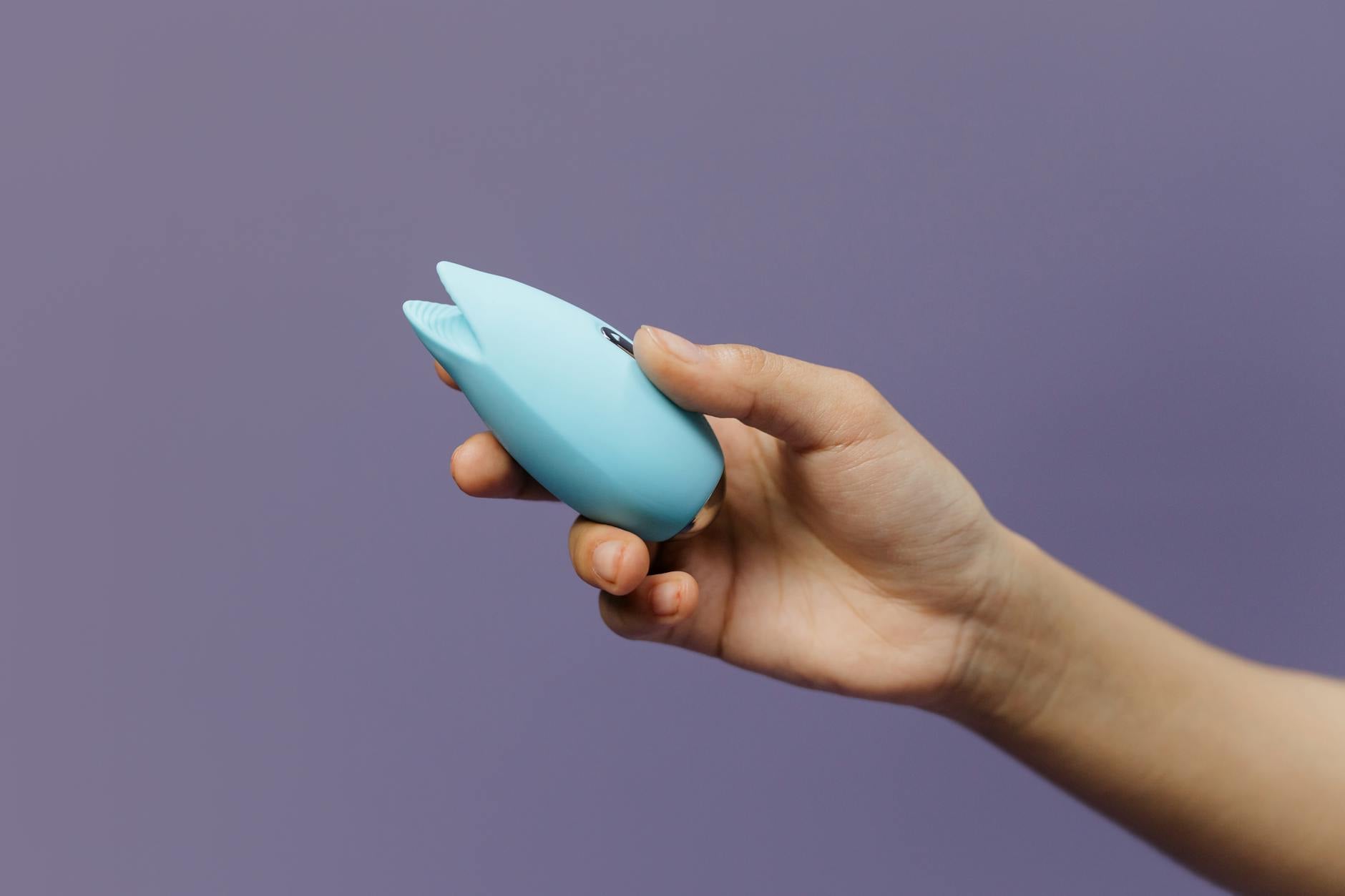 A hand holding a yellow silicone vibrator against a bright yellow background